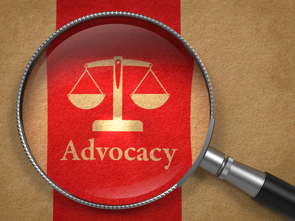 A magnifying glass over the justice scales and it says "Advocacy"